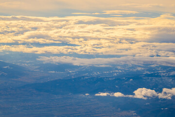 Fototapeta premium Vast clouds stretch over rolling mountains under a soft, golden light during sunset