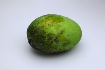 Close-up of a slightly damaged, unripened green mango on a white surface