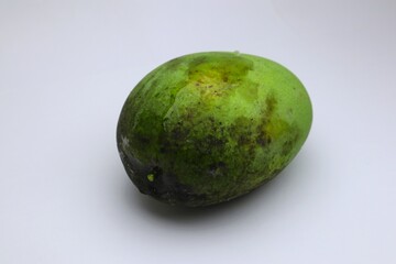 A Close-Up of an Unripe Mango with Visible Imperfections on a White Background