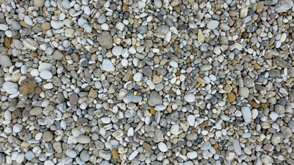 Background of small sea pebbles of various shapes and shades. Smooth and rough stones, natural texture, chaotic distribution.