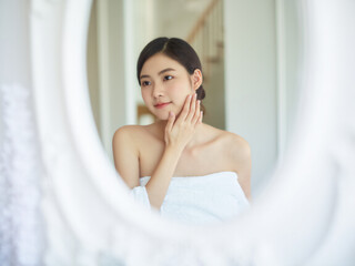 Naklejka premium A young woman in a white robe gently touching her face, showcasing a fresh and radiant complexion, symbolizing skincare, beauty, and self-care.