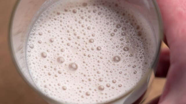 Hand holding a glass with frothy berry protein milkshake close up
