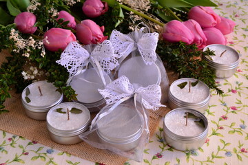 Wedding favors candle guest gifts bags with white lace bow, jute and pink tulips background, spring event party decoration handmade souvenirs