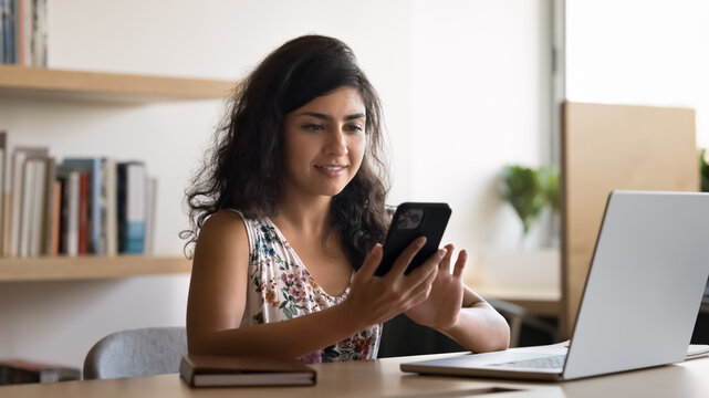 Multitasking in e-learning. Smiling young female student text message on smartphone screen before notebook confirm password to join virtual classroom for lecture get reminder for online learning task