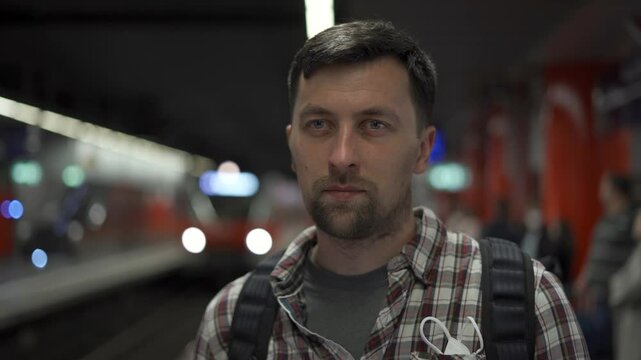 Young European man standing on platform of an S-Bahn station in Munich, Germany. He waits for his train in an urban setting, dressed casually. Scene captures daily commuting and city transport life. 