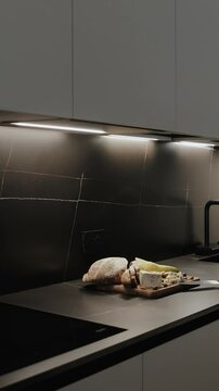 A black kitchen with a marble surface on which cheese, bread and grapes are flattering. 