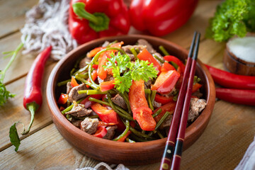 Chinese cuisine: salad with meat, vegetables and soy sauce in a plate on a wooden table for lunch. Chinese salad for dinner. Close-up.