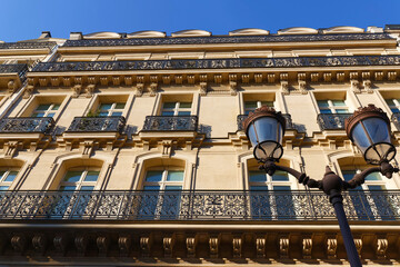Fototapeta premium Exterior architecture of Traditional French house with typical balconies and windows in Paris. Traditional Parisian street light in the foreground.