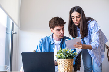 Worried people working from home, man analyzing numbers in notebook while woman behind observes...