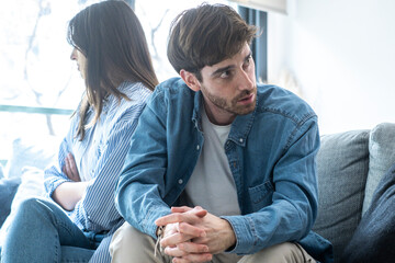 Upset couple sitting separately in their living room, ignoring each other, dealing with trust...