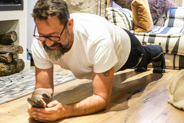 One adult man doing workout session at home in sportswear practicing plank exercise on the floor. A dog sleeping near him and a fireplace heat home. Concept of healthy lifestyle and training in midage