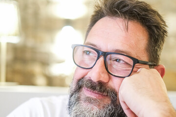 A middle-aged man, wearing glasses and a beard, smiles serenely while enjoying some quiet time alone in his cozy living room, feeling at peace in his surroundings and enjoying the calm atmosphere
