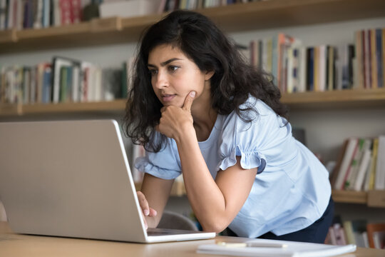 Digital age in education. Serious young woman high school student work on project in library use web resources databases to solve scientific problem participate in group research online via notebook