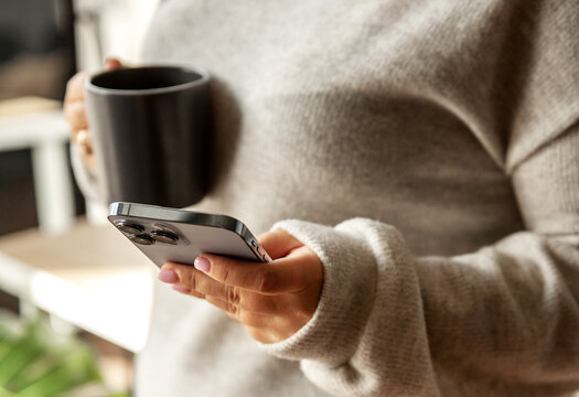 Woman holding a smartphone and coffee mug in cozy sweater