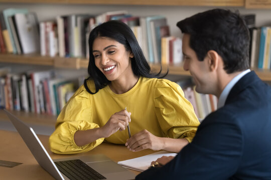 Collaboration in academic science. Young female student scientist meet with male peer tutor mentor colleague in public library discuss project research using laptop get professional work consultation
