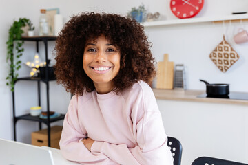 Young woman happily working from home in her cozy kitchen, exuding confidence and positivity with...
