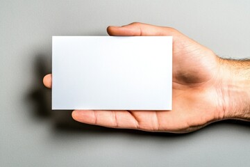 A hand grips a blank white business card set against a neutral background, perfect for showcasing branding or contact information