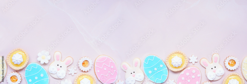 Poster Easter or spring themed baking bottom border with assorted cookies and sweet desserts. Top down view on a pink stone banner background with copy space.