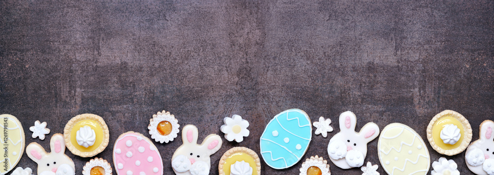 Aufkleber Easter or spring themed baking bottom border with assorted cookies and sweet desserts. Top down view on a dark stone banner background with copy space.