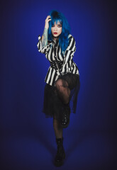 Studio portrait of freaky goth girl. Pretty blue-haired gothic lady in striped shirt, black skirt and tights
