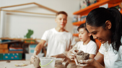 Caucasian boy modeling bowl of clay while cute asian girl working on dough at pottery workshop. Skilled highschool student playing on dough while wear muddy shirt at art lesson. Creative. Edification.