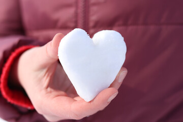Woman's hand holds snow in the shape of a heart. Winter. Close-up of woman's hands holding clean snow. Girl holding a snowball. Spending time outdoors in winter. Symbol of love. Valentine's Day
