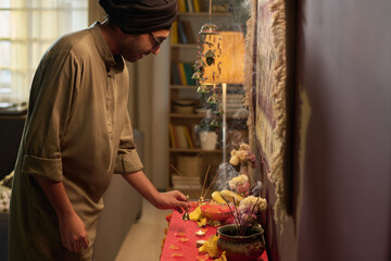 Man preparing religious altar with yellow candles and flowers in cozy indoor space. Focused and reverent setting displaying rituals and cultural practices