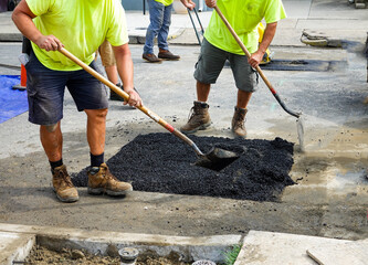 Two laborers filling i a hole in a asphalt street