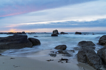 Lumière d’hiver sur la plage de Kerlouan, où les rochers sculptés par le temps émergent du sable. Pose longue sur une mer apaisée sous un ciel aux teintes pastel.