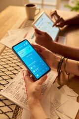 Hands holding smartphone and tablet while managing personal finances and analyzing expenses through...