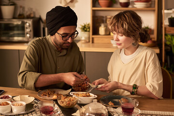 Two friends engaging in conversation while sharing food in a warmly lit kitchen filled with various dishes and utensils, creating a relaxed and intimate atmosphere