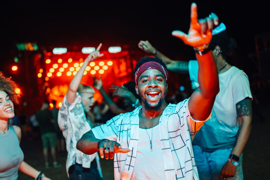 Excited young man dancing and enjoying live music at night concert with friends