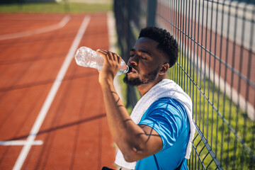 Young athlete drinking water after training on running track