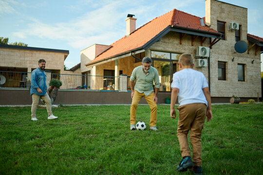 Happy family playing soccer in backyard of house - Powered by Adobe