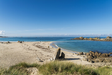 La plage des Amiets à Cléder s’étire en une longue bande de sable clair, ponctuée de rochers sculptés par le temps, sous un ciel bleu typiquement estival.