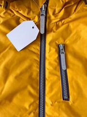 Label on clothes. New orange jacket with white price tag. Fragment of jacket with label, zipper, zippered pocket. Sewing clothes, production and sale of things