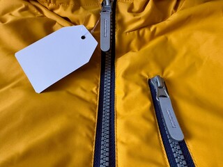 Label on clothes. New orange jacket with white price tag. Fragment of jacket with label, zipper, zippered pocket. Sewing clothes, production and sale of things