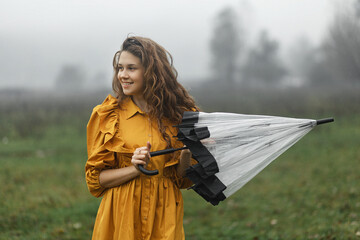 a woman with long wavy hair, wearing a bright yellow dress with ruffles on the shoulders. She is...