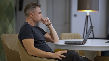 Thinking man contemplating at laptop in modern home