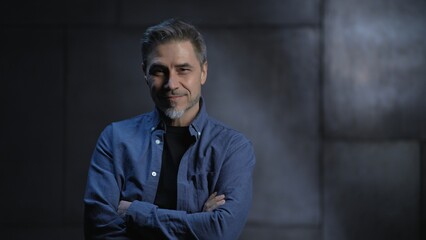 Portrait of happy mature casual man, smiling, standing in front of dark loft wall. Older, middle aged, mid adult, man in his 40s or 50s in shirt.
