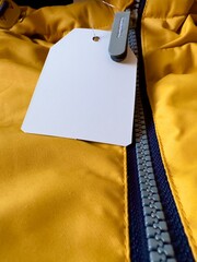 Label on clothes. New orange jacket with white price tag. Fragment of jacket with label, zipper, zippered pocket. Sewing clothes, production and sale of things