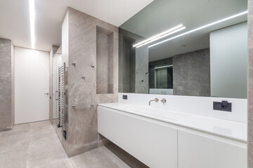 Luxury bathroom design decorated with beige marble tiles. Panoramic mirror over a white cabinet with a sink.