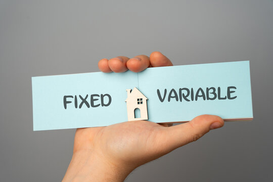 Mortgage rates, loan and real estate concept. The inscription Fixed and Variable on a notebook in the hands of a man and a miniature house.