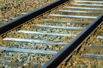Metal railway tracks are lined with gravel, stretching across the countryside under clear blue...