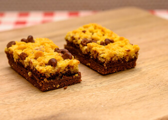Chocolate chip cookie bars are sitting on a wooden countertop, showcasing a golden yellow crust and chocolate morsels. Perfect for sharing during gatherings or dessert cravings