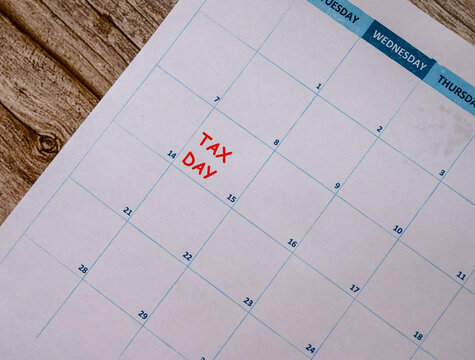 A calendar sheet displays the date marked in red as tax day, set against a textured wooden background. The month is visible, highlighting the importance of deadlines