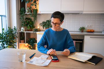 Focused serious woman accountant using smartphone, reviewing finances and managing bills. Working...