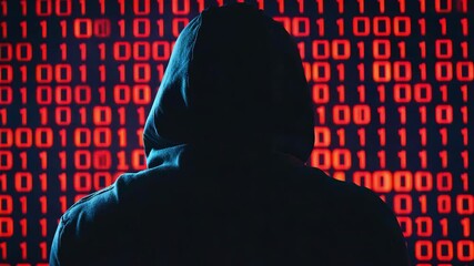 A silhouette of a hacker stands in front of glowing red binary code on a black screen. Cyber attack concept - Powered by Adobe