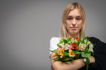 Portrait of a young, emotional girl with a bouquet of fresh spring flowers, smiling and excited. Studio shot with soft lighting and a neutral background that conveys emotions and natural beauty