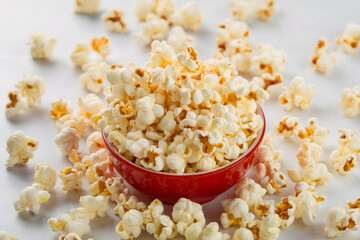 Overflowing Red Bowl of Fresh Popcorn with Scattered Kernels on a White Background
